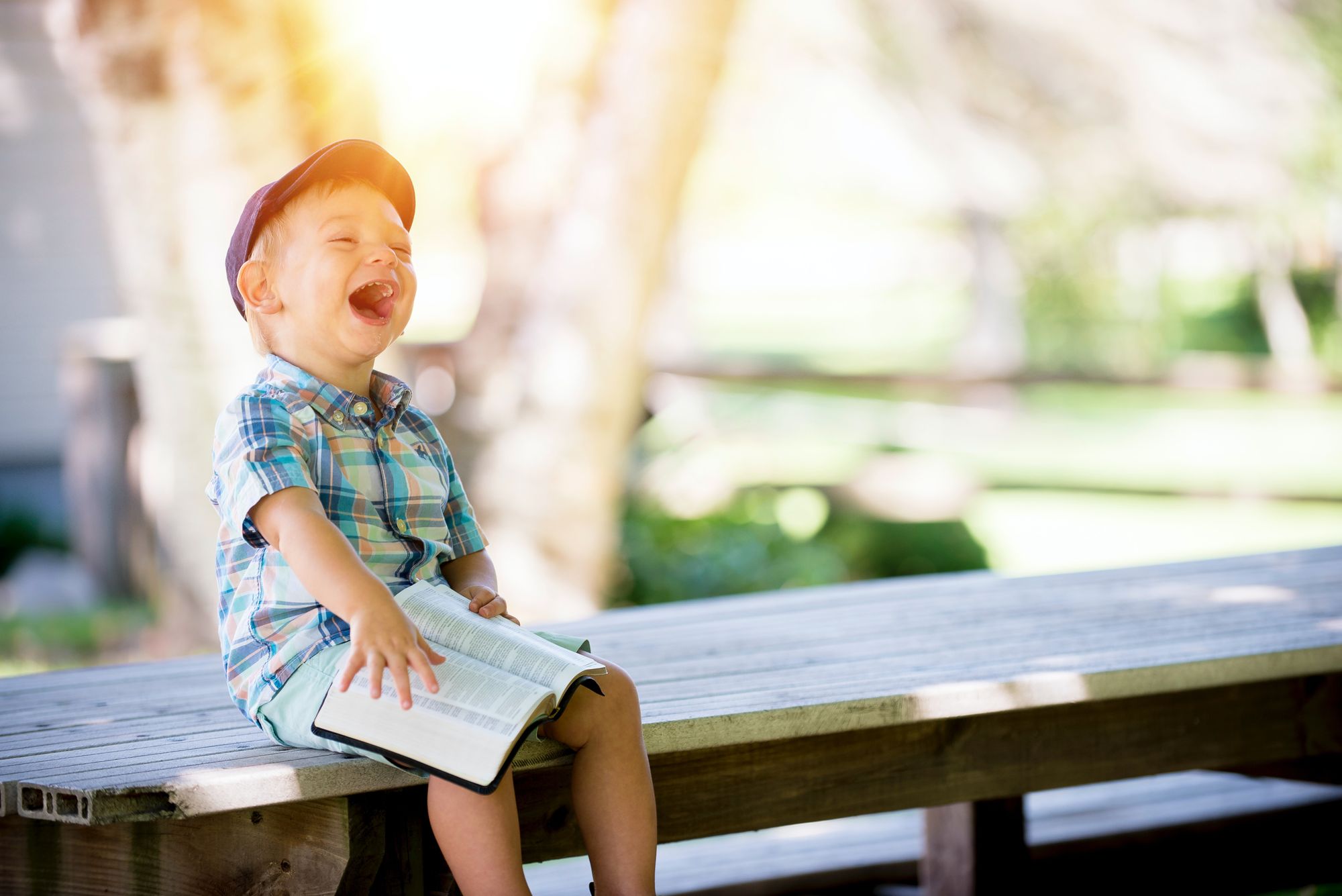 Young boy, with book open, laughing while sitting on picnic table