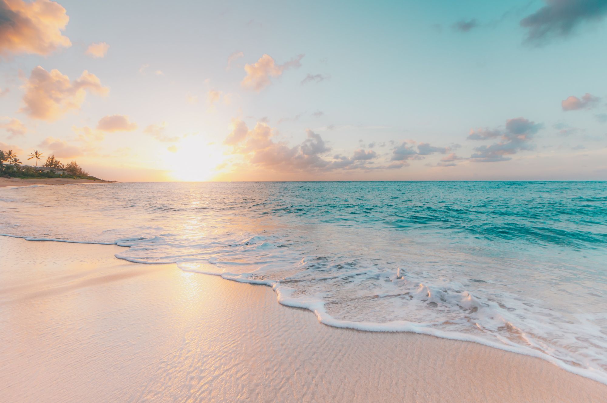 Beach with white sand and brilliant blue water, with bright sunrise in background with a few clouds
