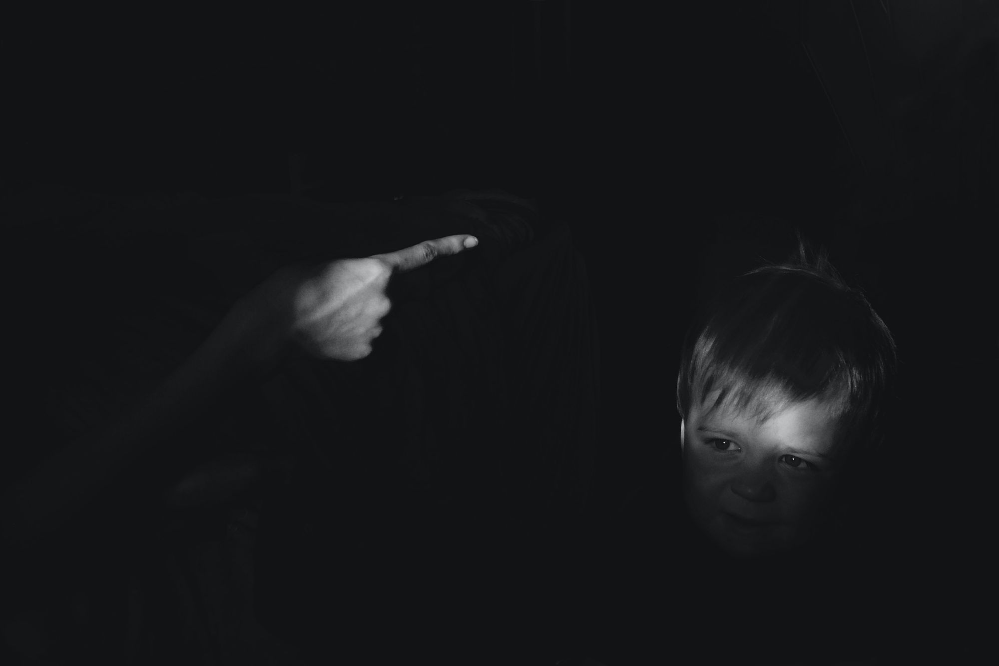 Black & white photo of child's face and adult pointing at him